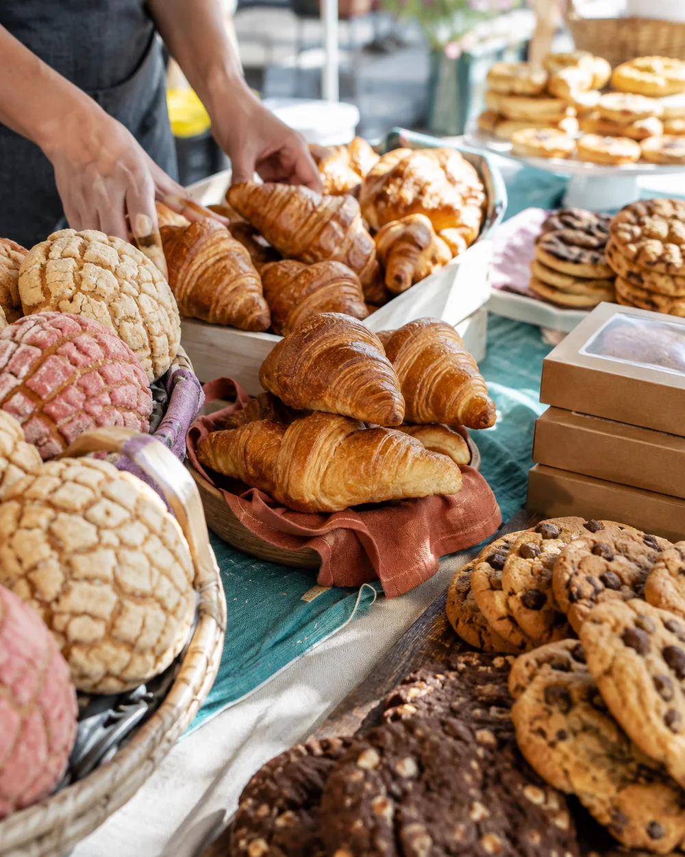 Illustrative baker arranging conchas, croissants, and cookies at a market table
